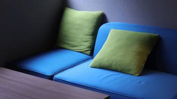 A blue sofa with green cushions in a room with a wooden table and a grey wall.