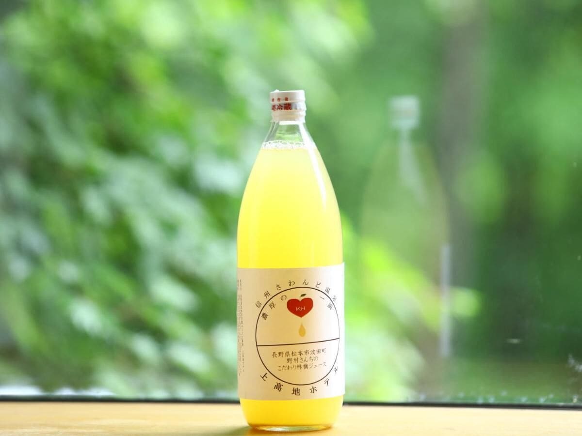 A bottle of yellow liquid with a label featuring a heart and Japanese text, placed on a wooden surface with a blurred green background.