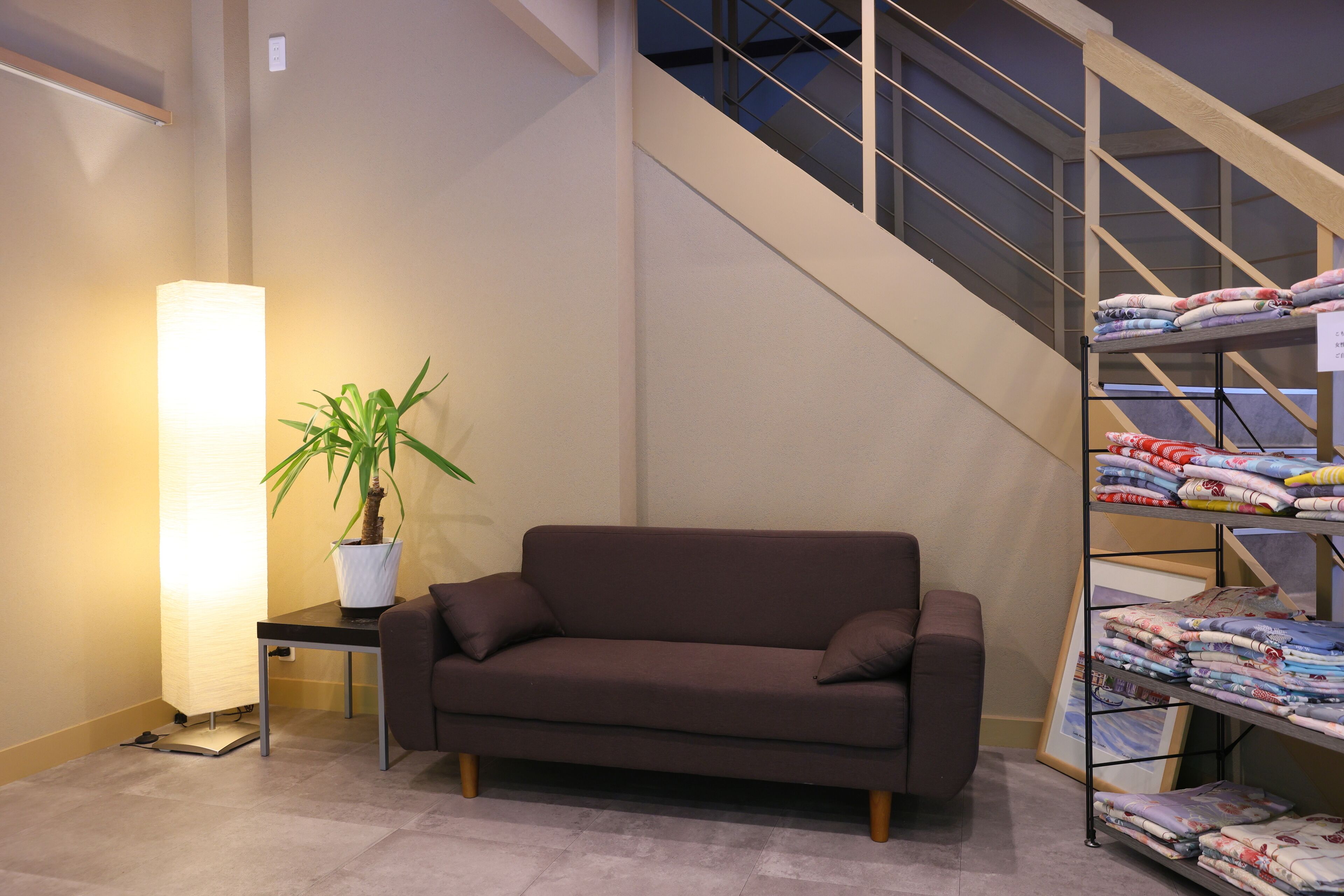 Un intérieur moderne avec un canapé marron, une plante en pot, une lampe et un escalier.