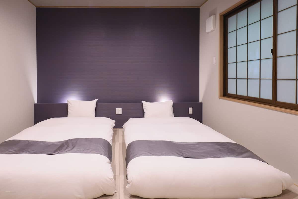 A twin room with two beds, a dark headboard, a window with a grid pattern, and a wall-mounted air conditioner.