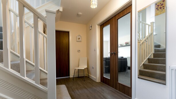 A hallway with a wooden floor, white walls, and a bench. There is a door with a mirror and a picture frame on the wall. - KVM - Quayside House (Peterborough)