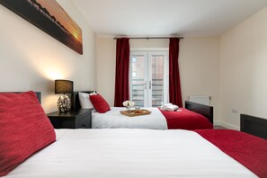 A hotel room with two beds, red bedding, a tray with flowers, a lamp, and a painting on the wall. - KVM - Quayside House (Peterborough)