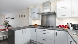 A modern kitchen with white cabinets, a stainless steel stove, and a red coffee maker. - KVM - Quayside House (Peterborough)
