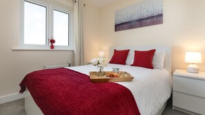 A neatly made bed with a red blanket, a tray with pastries and flowers, and a painting on the wall. - KVM - Quayside House (Peterborough)