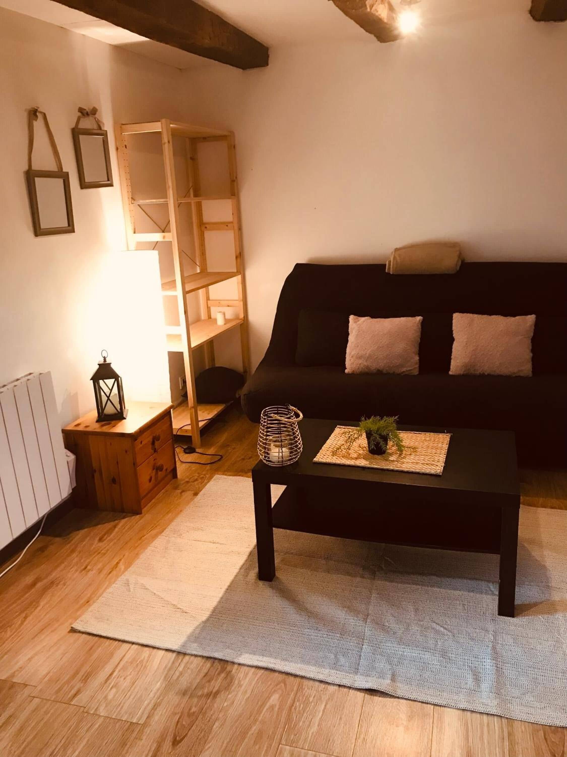Uma sala de estar acolhedora com um sofá preto, mesa lateral de madeira e uma mesa de centro com uma planta.