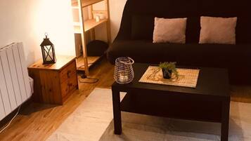 Uma sala de estar acolhedora com um sofá preto, mesa lateral de madeira e uma mesa de centro com uma planta.
