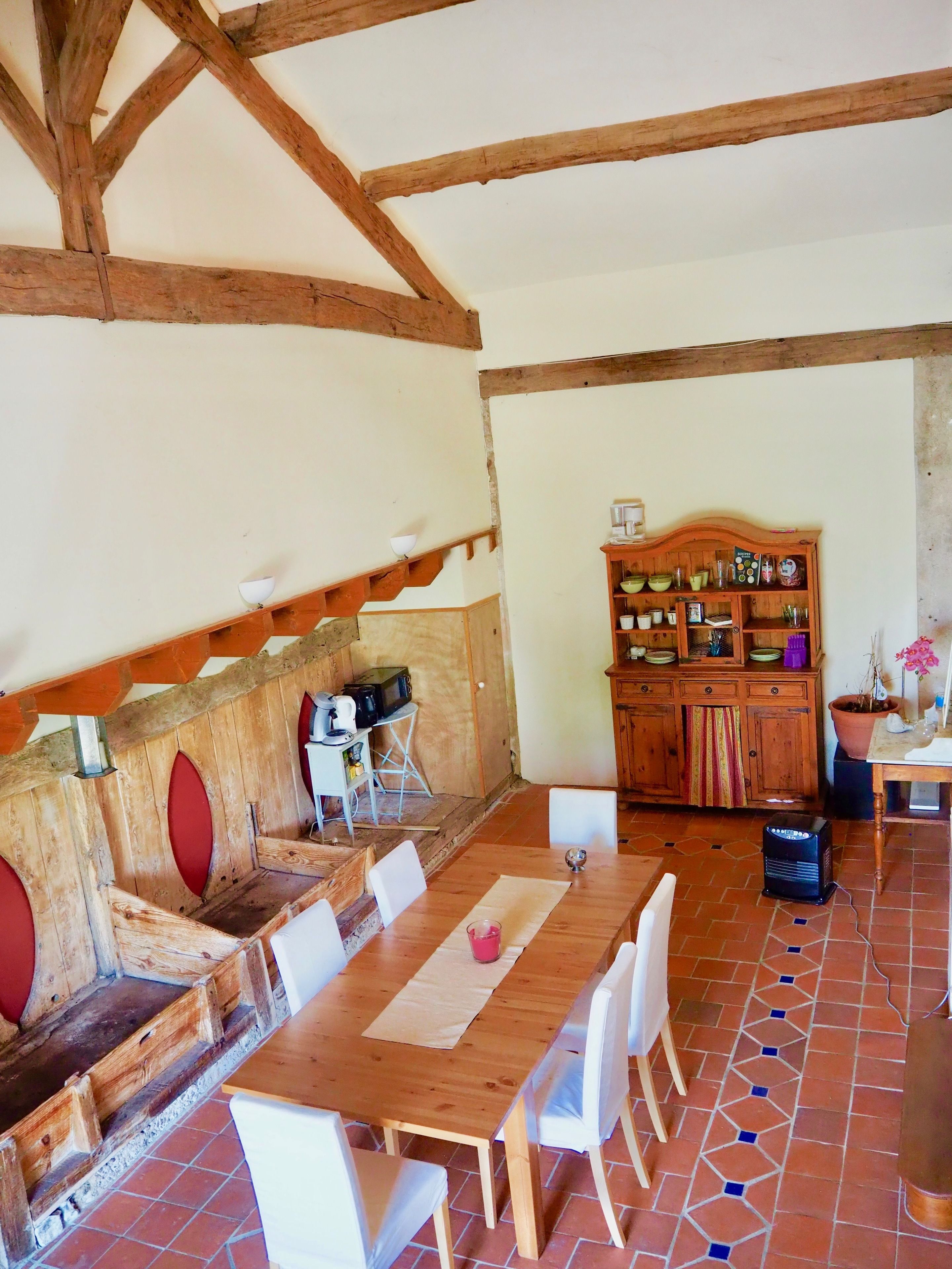 Un comedor rústico con una mesa y sillas de madera, un aparador de madera con utensilios de cocina y un piso de baldosas.