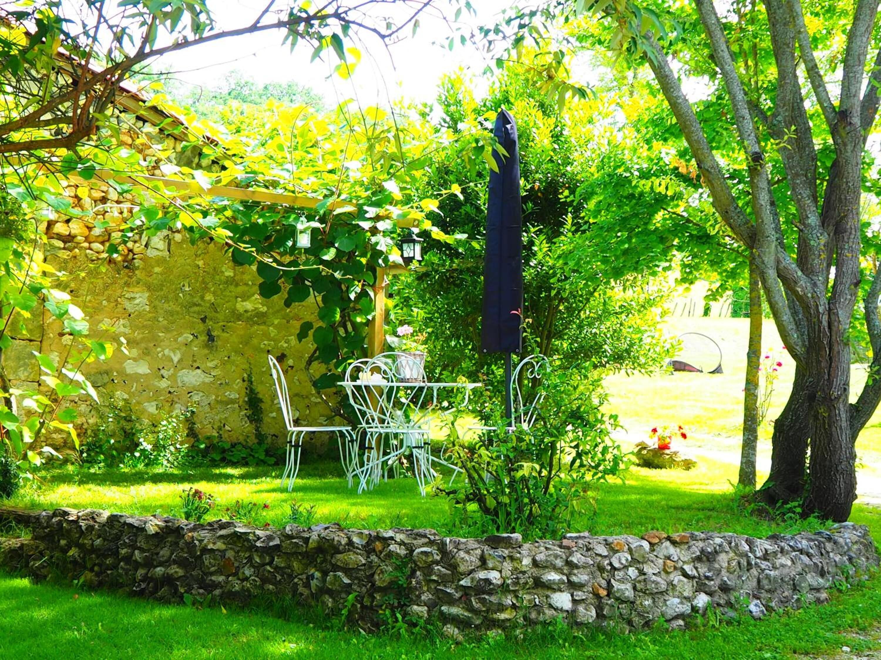 A stone wall, a metal table with chairs, and a tree in a garden.