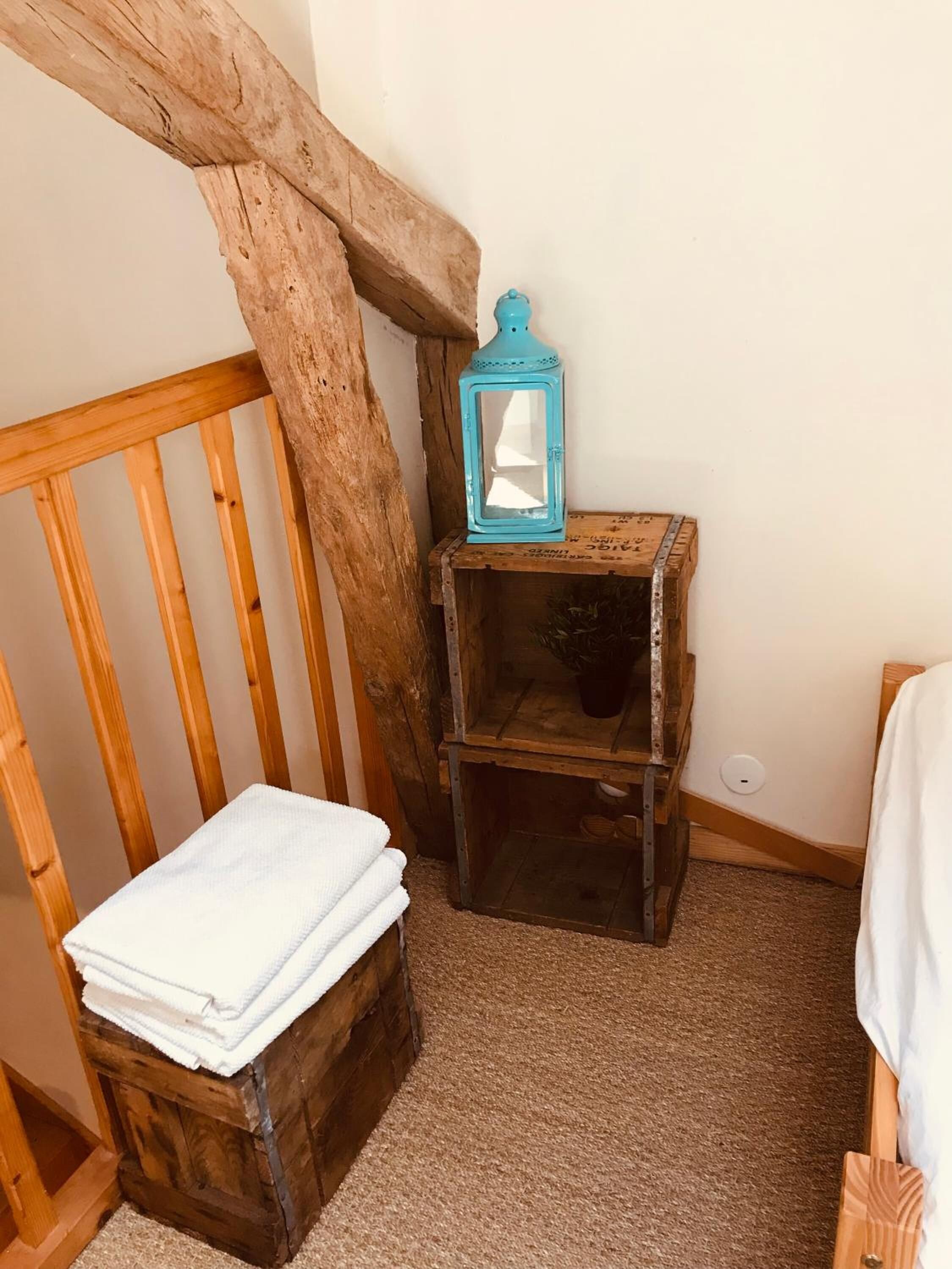 Une pièce rustique avec un banc en bois, une petite table en bois sur laquelle est posée une lanterne, et une serviette blanche sur une commode en bois.