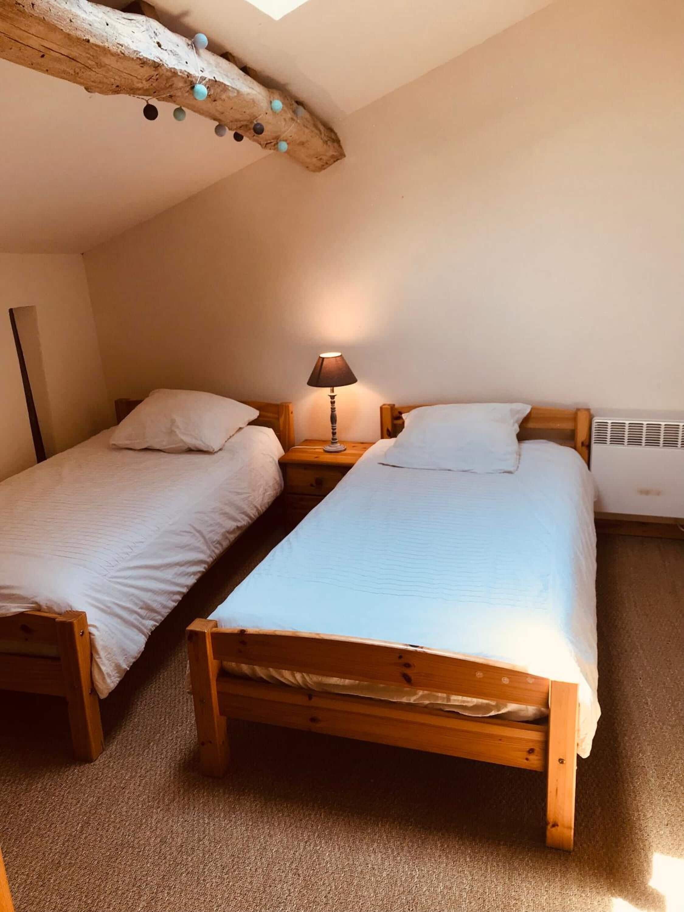 Una habitación pequeña y acogedora con dos camas de madera, una mesita de noche con una lámpara y un techo inclinado con vigas a la vista.
