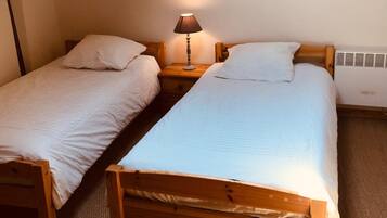 Una habitación pequeña y acogedora con dos camas de madera, una mesita de noche con una lámpara y un techo inclinado con vigas a la vista.