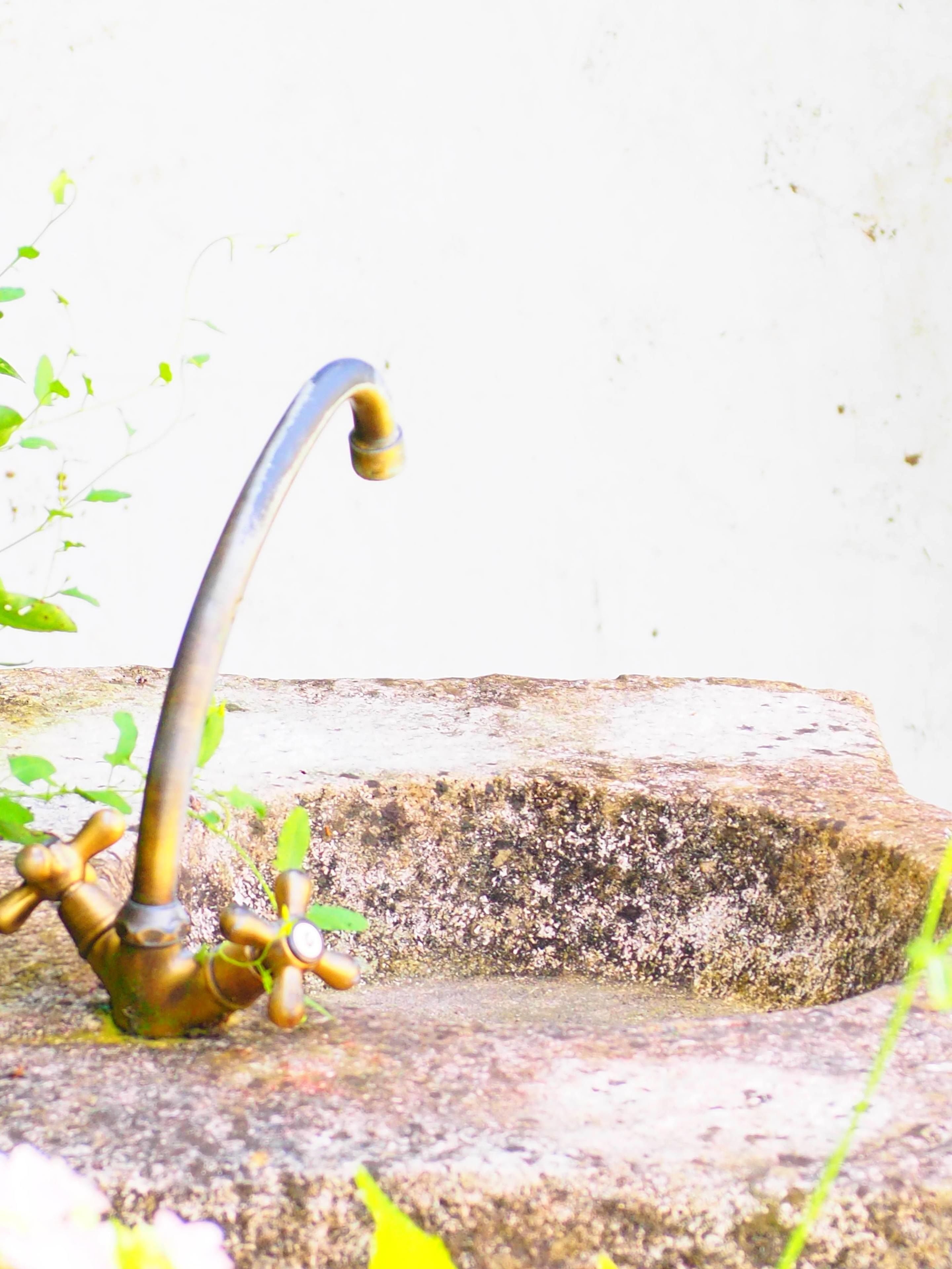 Ein alter Messing-Wasserhahn mit mehreren Griffen, an einem Steinsinkwanne befestigt.