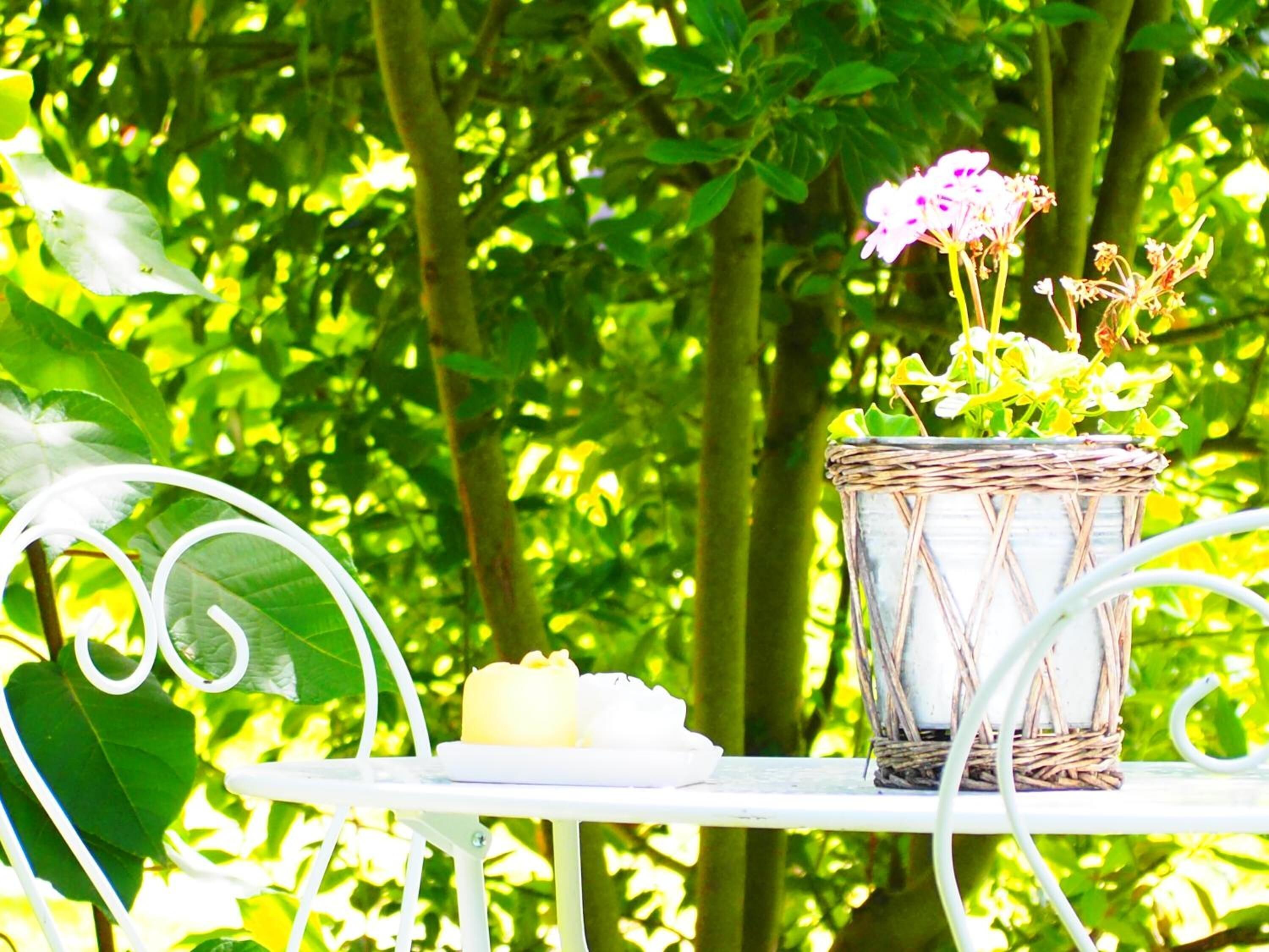 A wicker basket with flowers and candles on a white metal table outdoors.