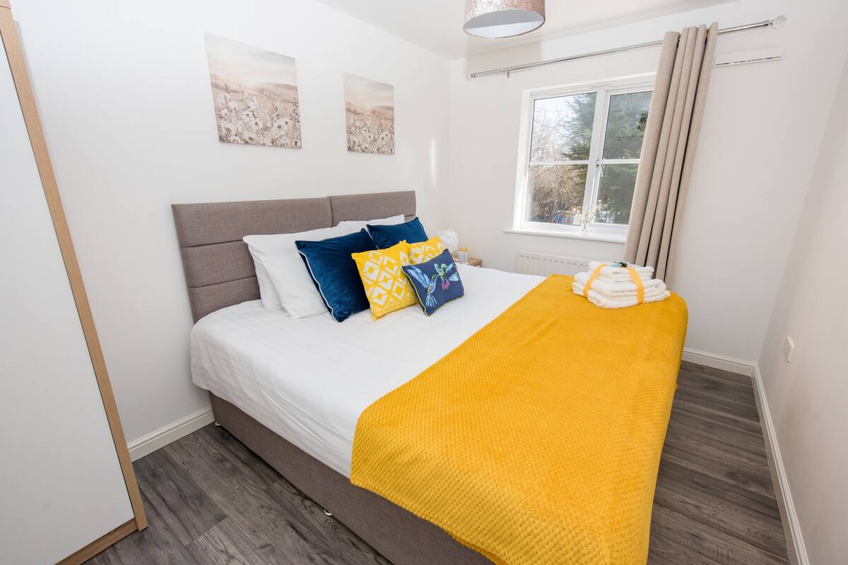 A neatly made bed with a white and yellow blanket, a grey headboard, and decorative pillows.