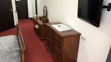 A bedroom with a bed, wooden dresser, a mirror, and a TV mounted on the wall.