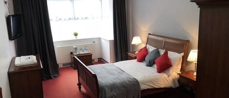 A hotel room with a bed, bedside tables, a TV, a window with curtains, and a view of the outside.