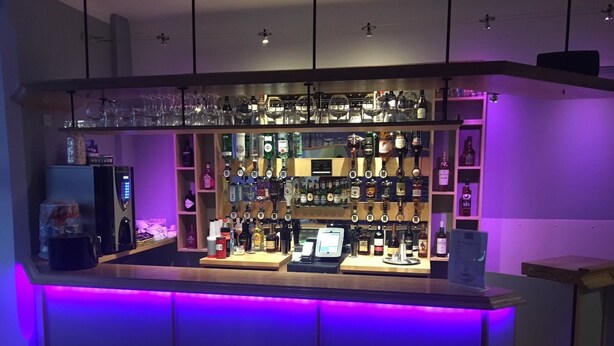 A bar area with shelves of liquor bottles, a coffee machine, and a cash register.