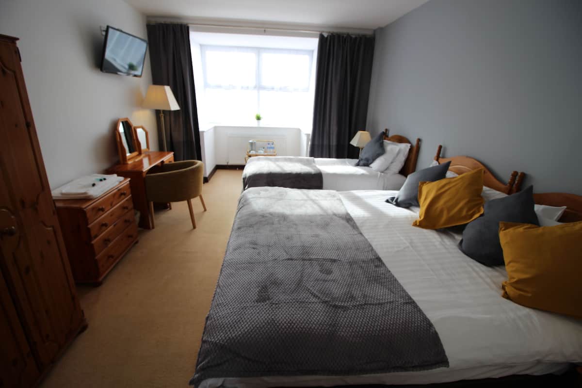 A hotel room with two beds, a desk, a chair, a television on the wall, and a window with curtains.