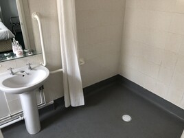Un baño con lavamanos blanco, una repisa de vidrio con artículos de aseo y una cortina de ducha.