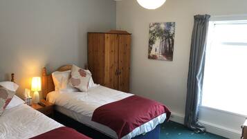 A bedroom with two beds, a wooden wardrobe, a painting, and a window with curtains.