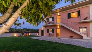 Una casa de dos pisos con un sendero de piedra que lleva a la entrada, un balcón con mobiliario exterior y una escalera al piso superior.