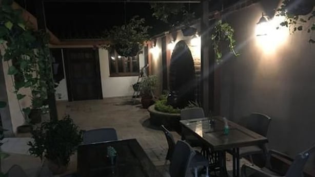 An outdoor patio area with a table and chairs, surrounded by potted plants and a wall with hanging lights. - Hostal Tía Mema (Santa Ana)