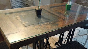 A glass-top dining table with chairs, a small potted cactus, and a green container. - Hostal Tía Mema (Santa Ana)