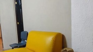A yellow sofa in a room with a white wall and a small decorative angel figure next to it. - Hostal Tía Mema (Santa Ana)