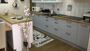 Una cocina moderna con armarios blancos, un microondas, un fregadero y una cafetera. Hay una planta ornamental de orquídea en la encimera y una alfombra estampada en el suelo.