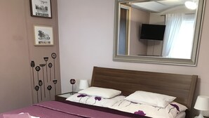 Una cama bien hecha con una colcha morada y almohadas blancas, un cabecero de madera, un espejo grande y cuadros en la pared.