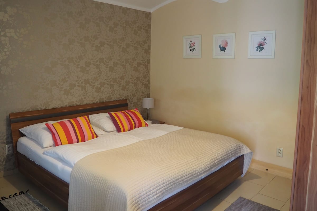 Ein Schlafzimmer mit einem Bett, einem Nachttisch, einer Lampe und Wandbildern mit floralem Muster.