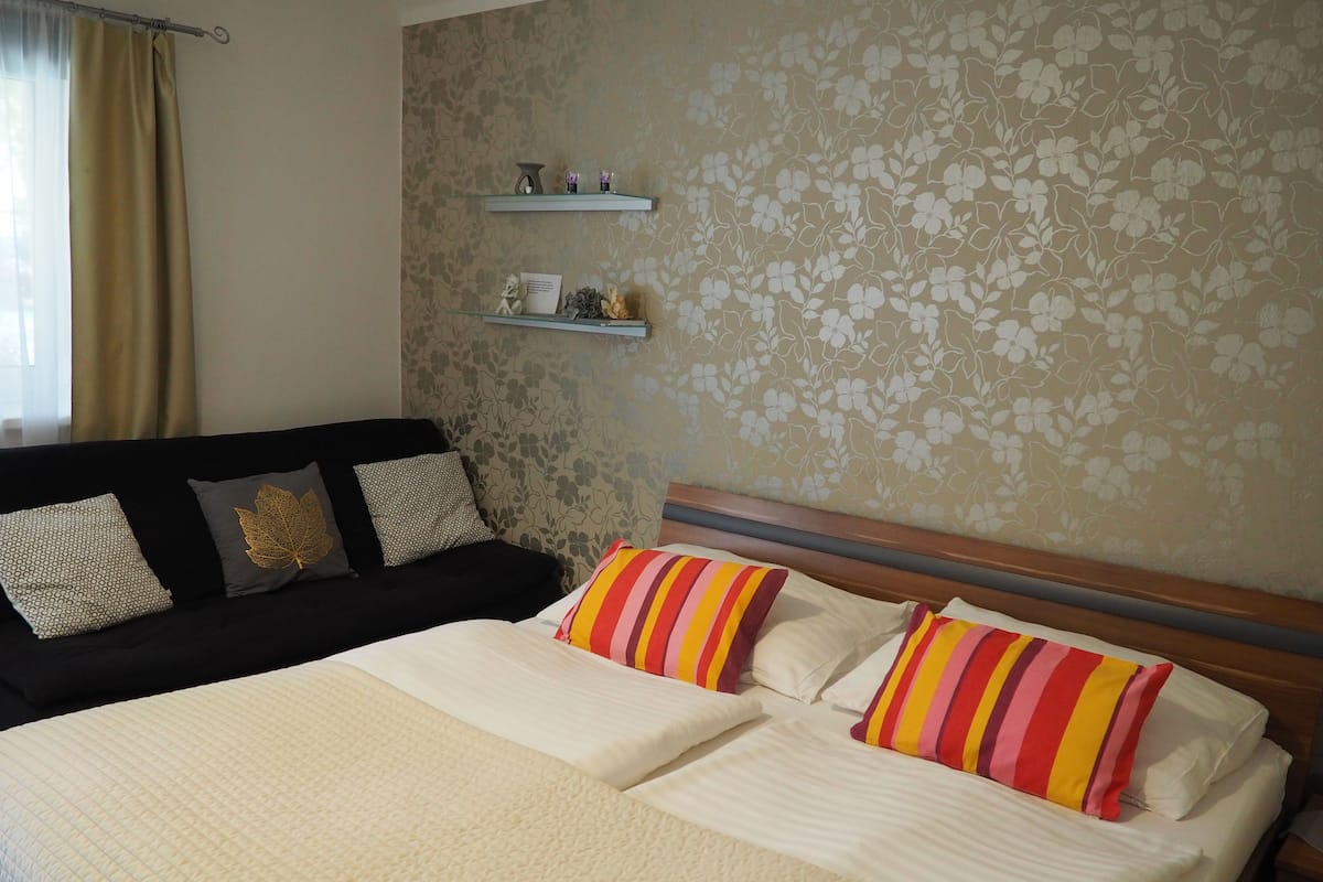 Ein Hotelzimmer mit einem Bett, einer schwarzen Schlafsofa und einer Wand mit Blumenwallpaper.