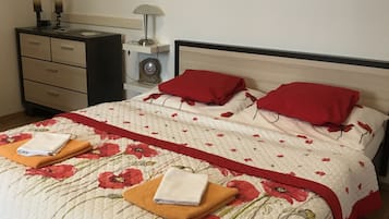 Un letto rifatto con cura, coperta floreale, due cuscini rossi e due asciugamani piegati.