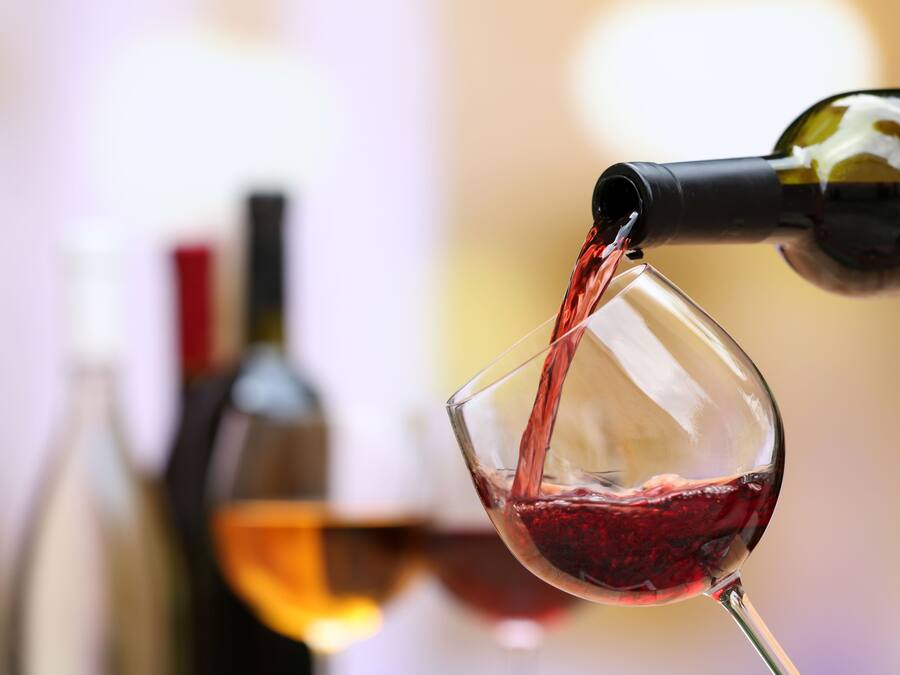 Una botella de vino vertiendo vino tinto en una copa.