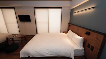 Een moderne hotelkamer met een groot bed, een klein rond tafeltje, een flatscreen televisie aan de muur en een schuifdeur.