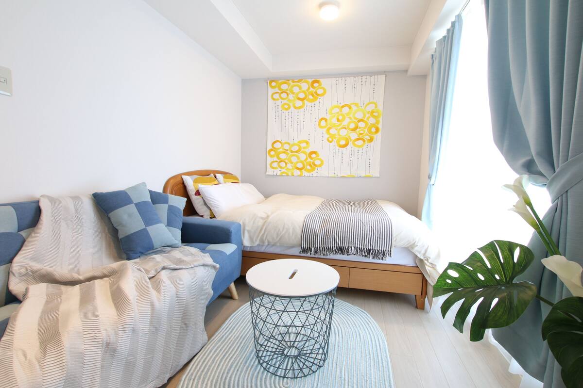 A modern bedroom with a bed, a sofa, a round side table, and a large window with curtains.