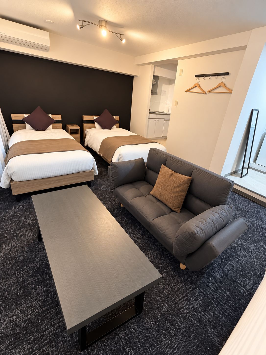 Habitación de hotel con dos camas, un sofá, una mesa y vistas a una cocina.