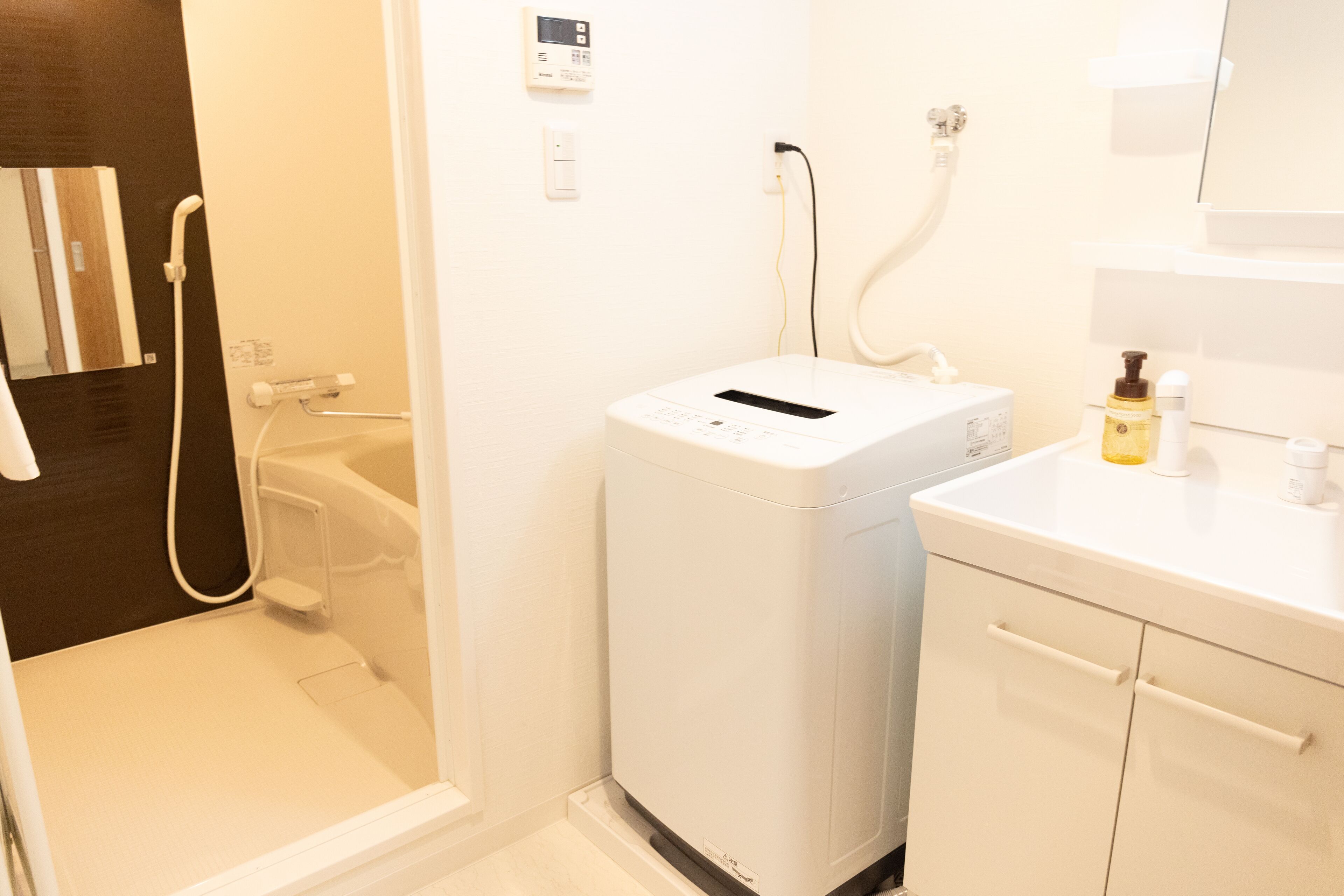 A compact, modern bathroom with a built-in washer and dryer, a small sink, and a mirror above the counter.