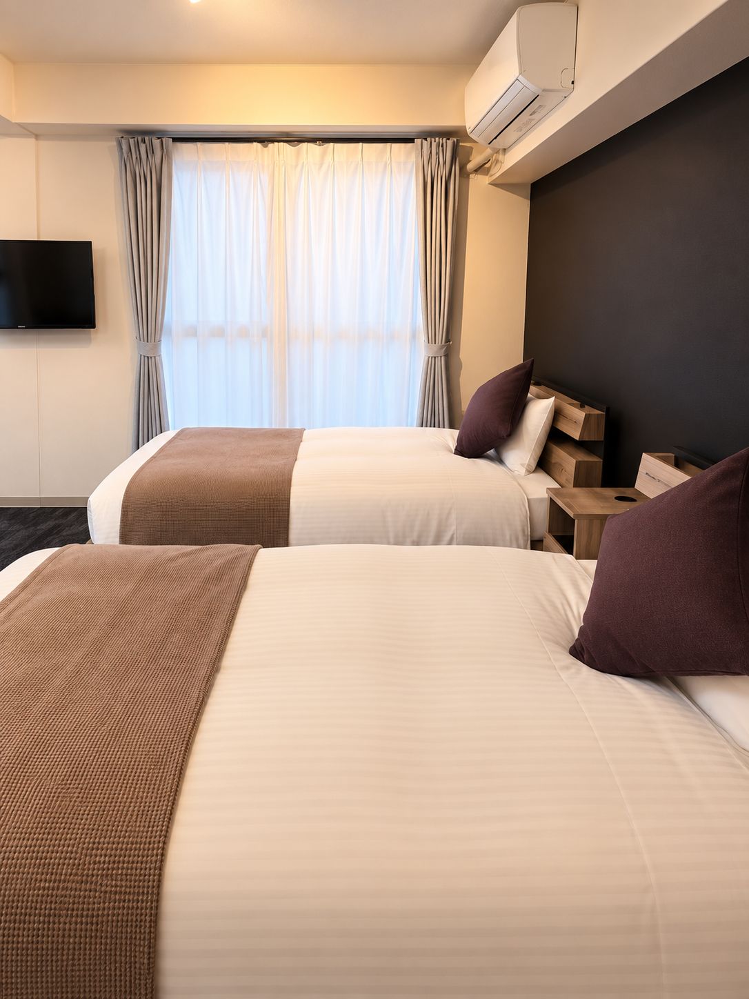Quarto de hotel com duas camas, televisão de tela plana, aparelho de ar condicionado e janela com cortinas.