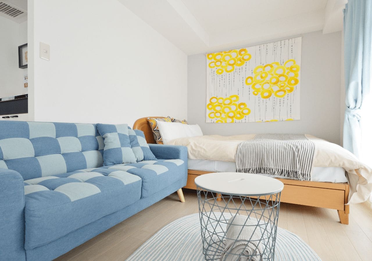 Een moderne woonkamer met een blauwe bank, een ronde salontafel en een bed met een gestreept dekbed.
