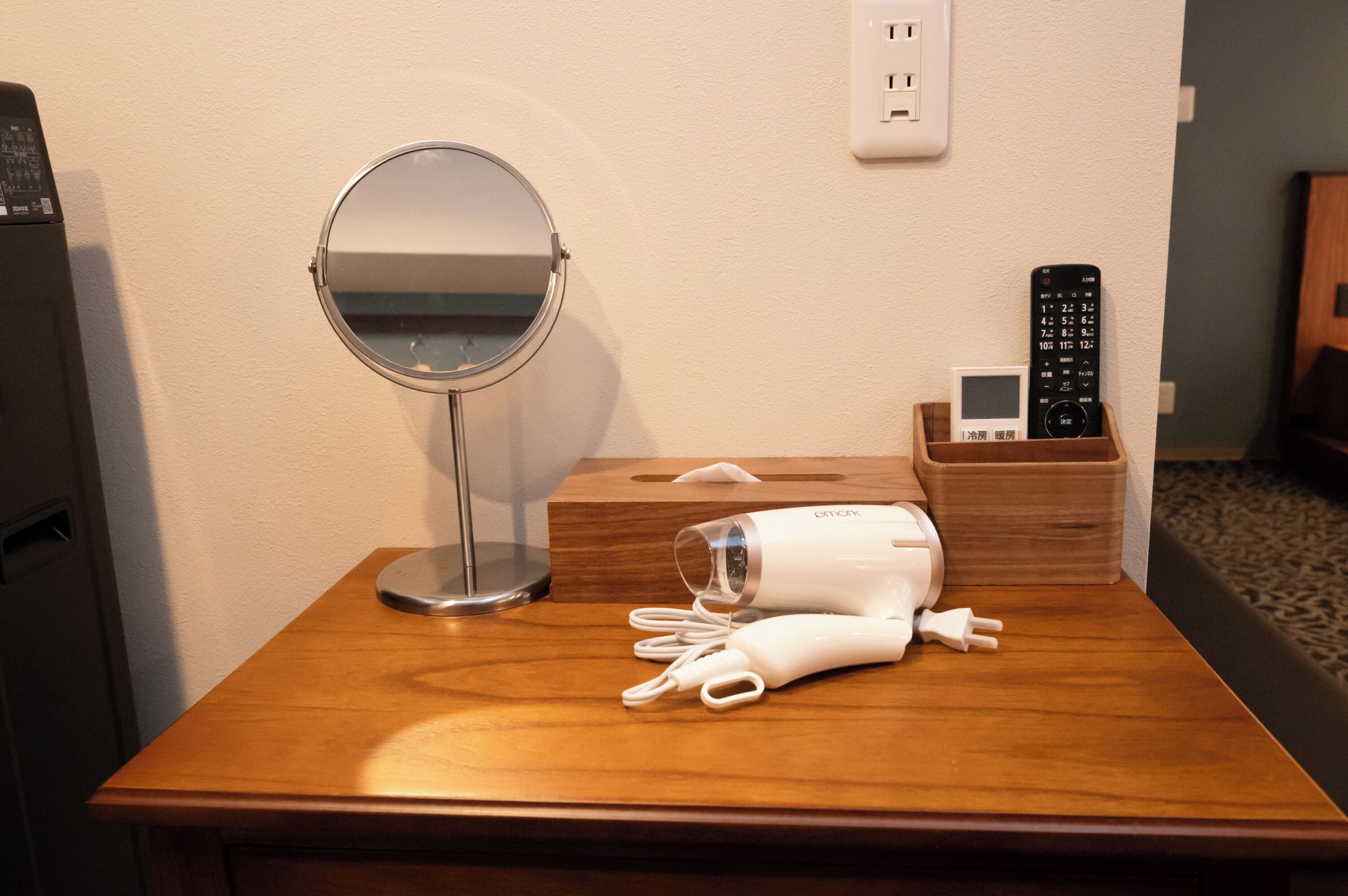 A wooden table with a round mirror, a white hairdryer, and a remote control in a wooden holder.