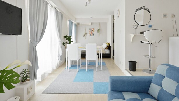 A modern living room with a blue sofa, a dining area with a white table and chairs, and a kitchen area with a white fridge. - KIKU'S ROOM (Osaka)