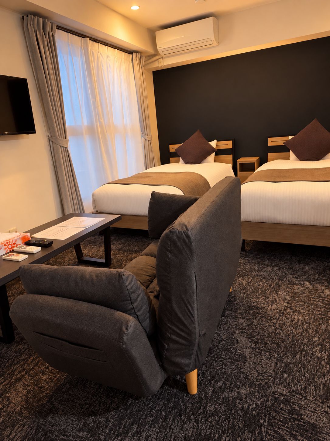 Ett hotellrum med två sängar, ett skrivbord och en luftkonditioneringsanläggning.