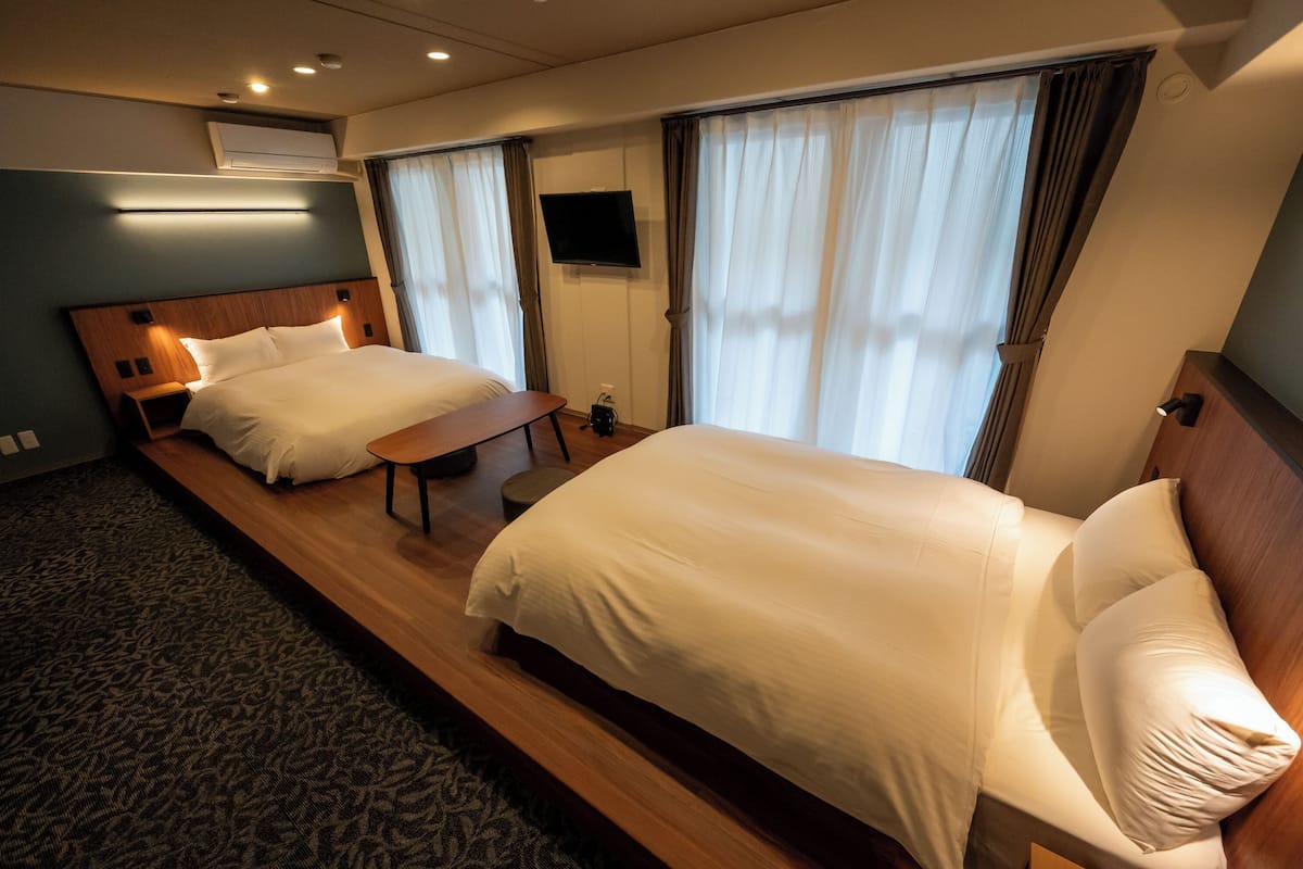 A hotel room with two beds, a flat-screen TV, and a small table.