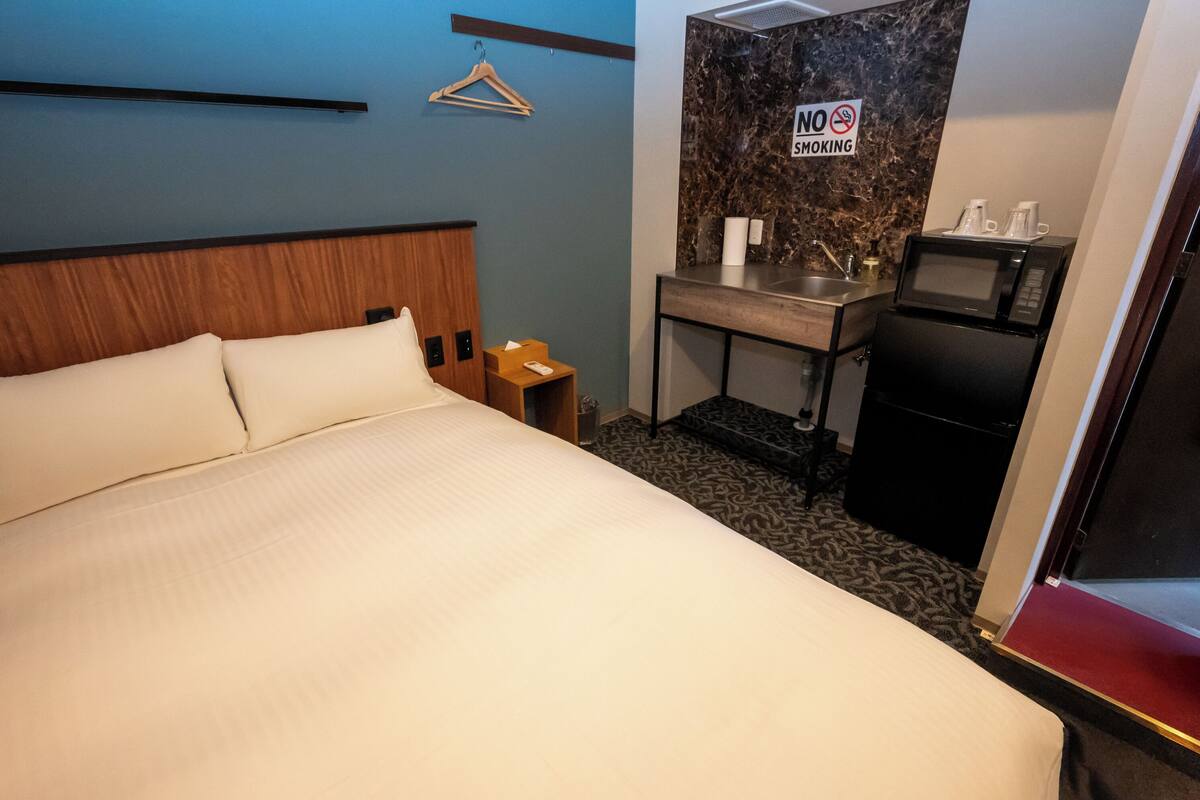A hotel room with a bed, a small desk with a sink, a microwave, and a 'No Smoking' sign.
