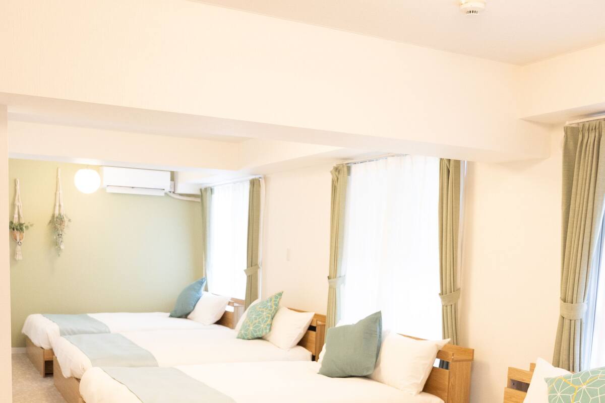 A hotel room with three beds arranged in a row, each with a wooden headboard and a light-colored bedspread.