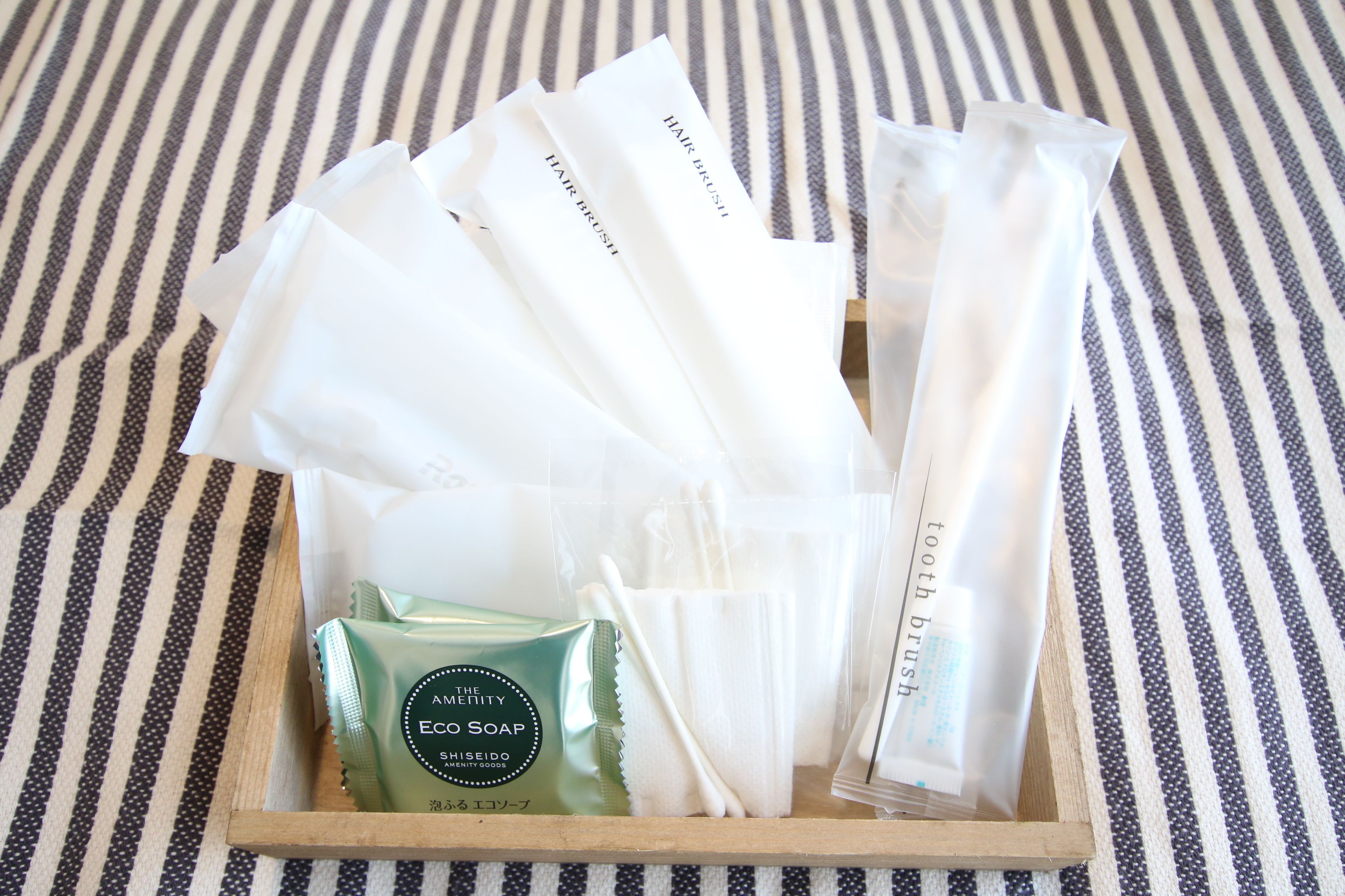A wooden tray with various toiletries including a green soap bar, white toothbrushes, and a tube labeled "tooth brush".