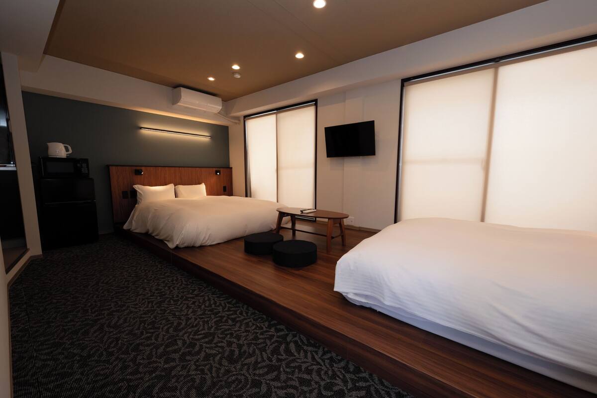 A hotel room with two beds, a small table, a flat-screen TV, and a microwave.