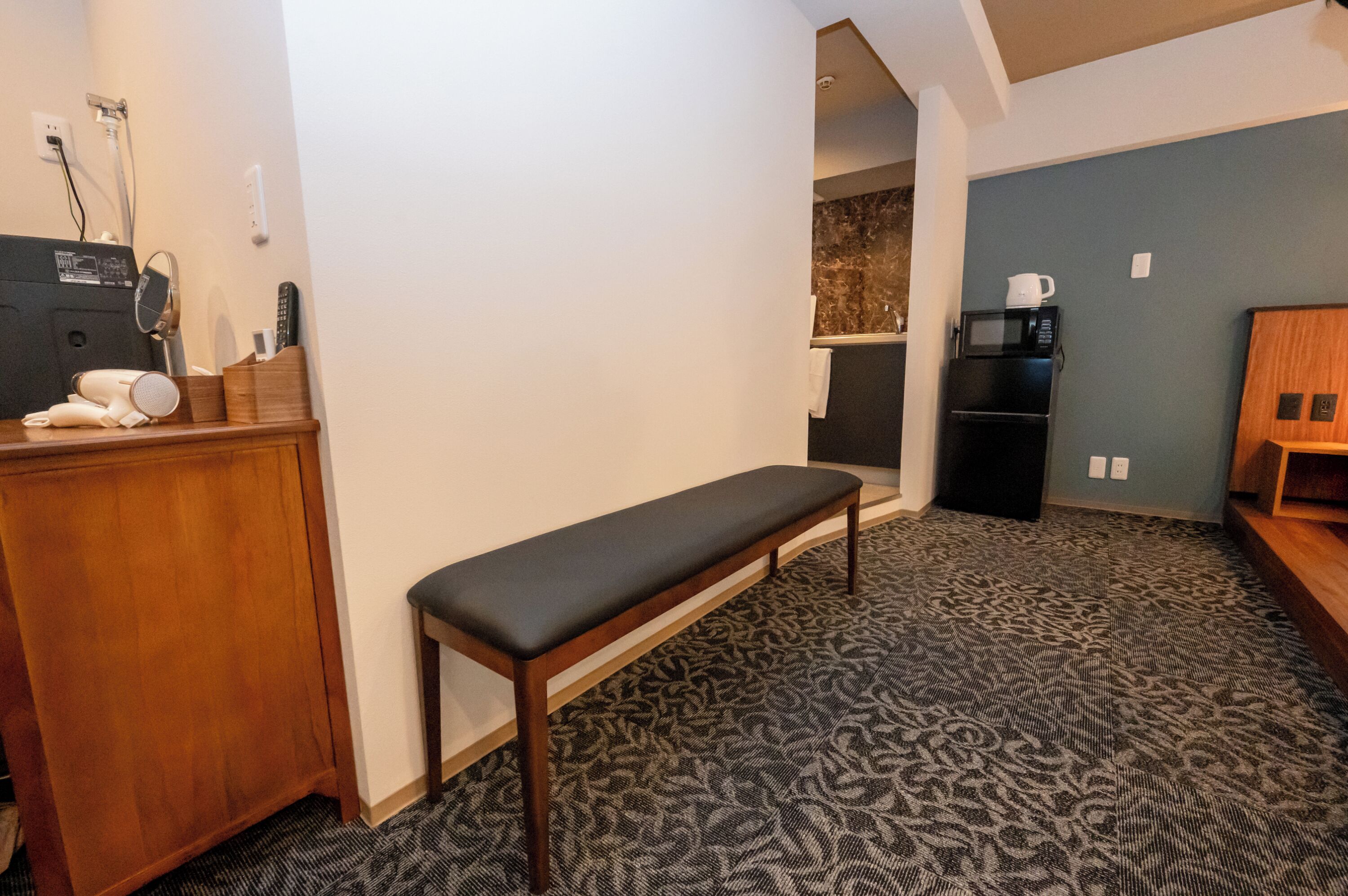 A room with a bench, a wooden desk, a microwave, and a coffee machine.