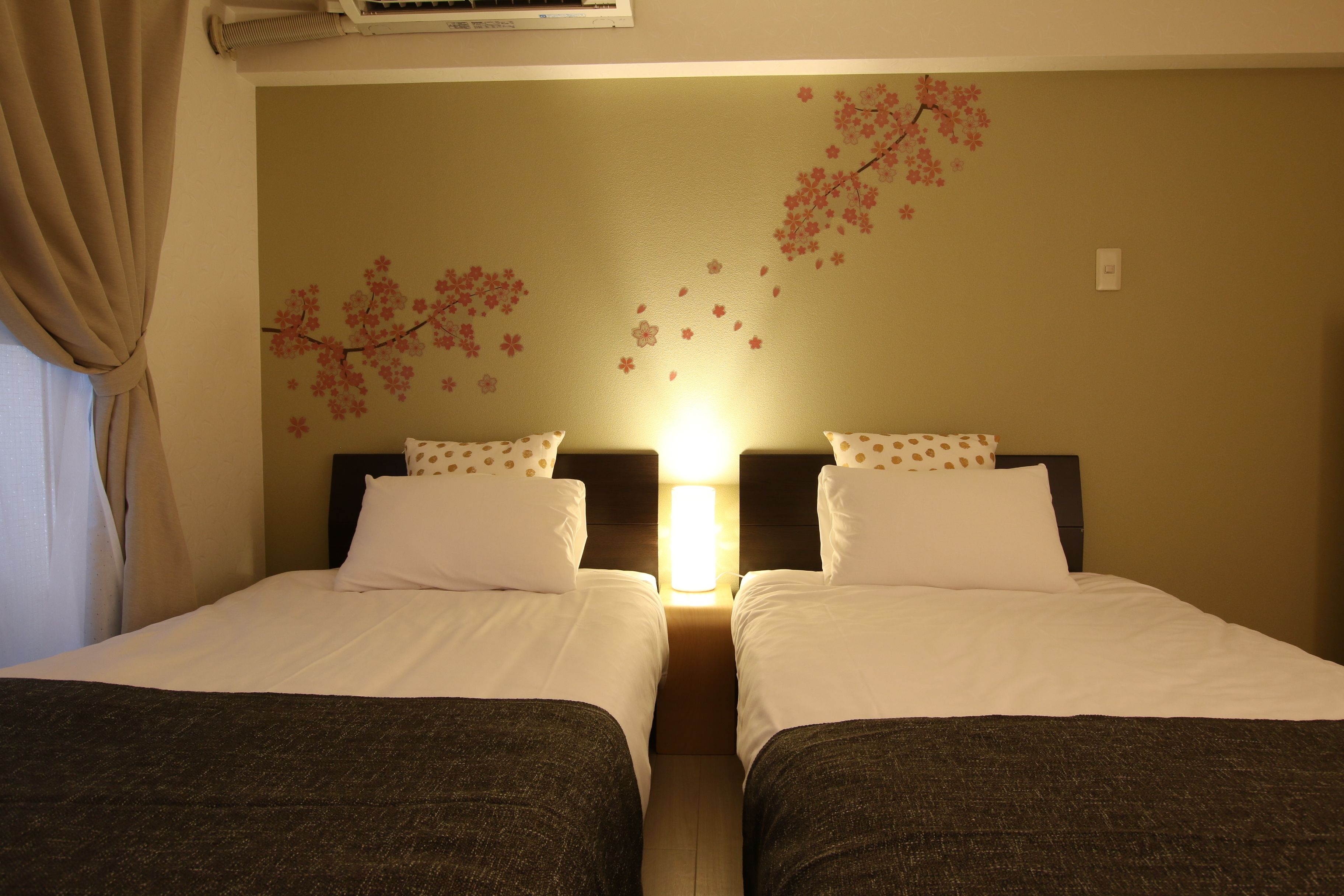 Camera d'albergo con due letti, condizionatore d'aria a muro e un quadro decorativo con fiori di ciliegio.
